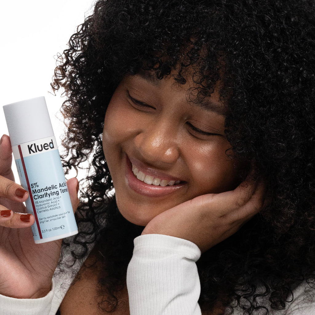 Woman holding a bottle of Klued skincare product with a neutral background