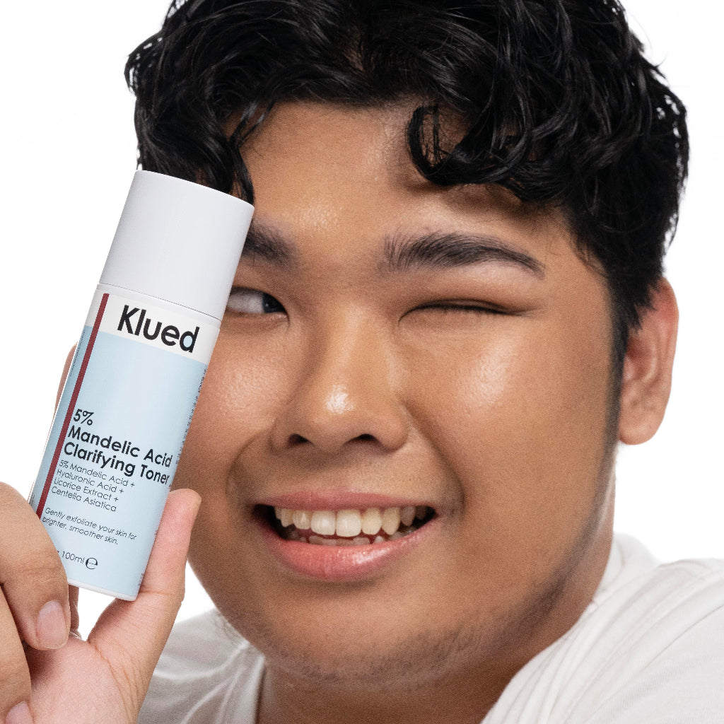 Person holding a Klued skincare product near their face on a white background