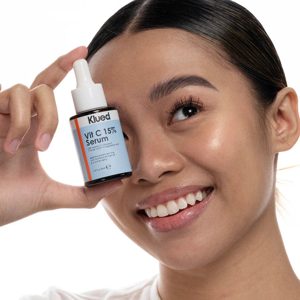Woman holding a bottle of Klued Vitamin C 15% Serum close to her face.