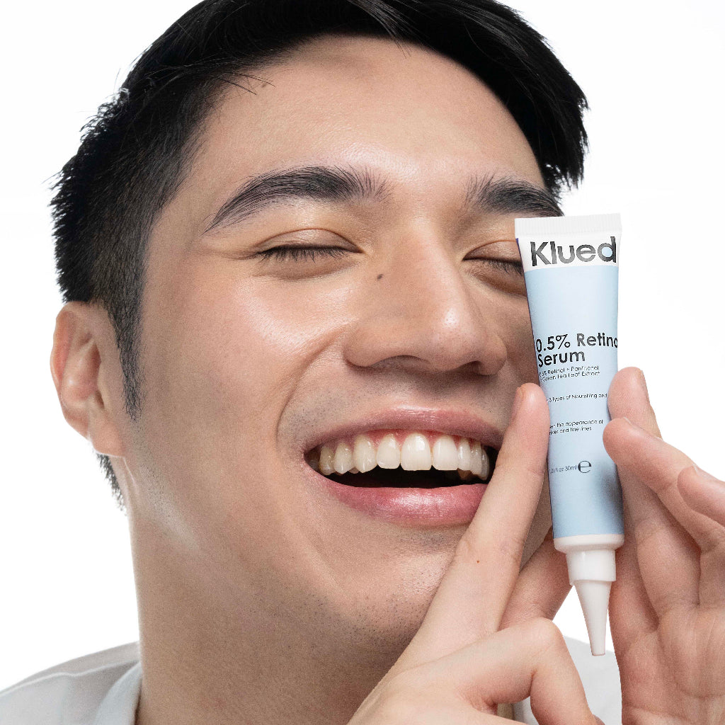 Man holding a tube of Klued 0.5% Retinol Serum close to his face.