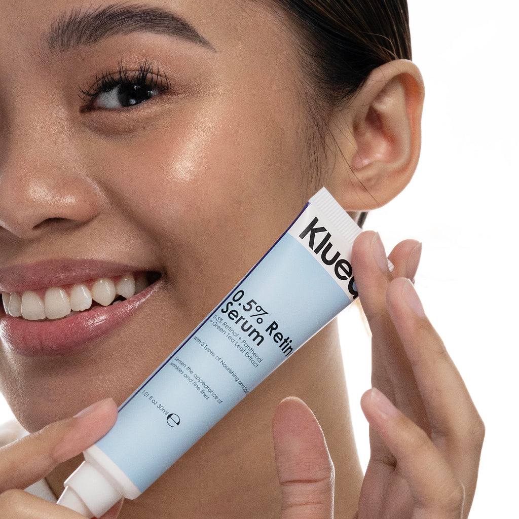 Woman holding a Klue serum tube close to her face on a white background
