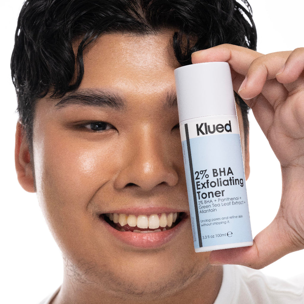 Person holding a bottle of Klued 2% BHA Exfoliating Toner close to their face.