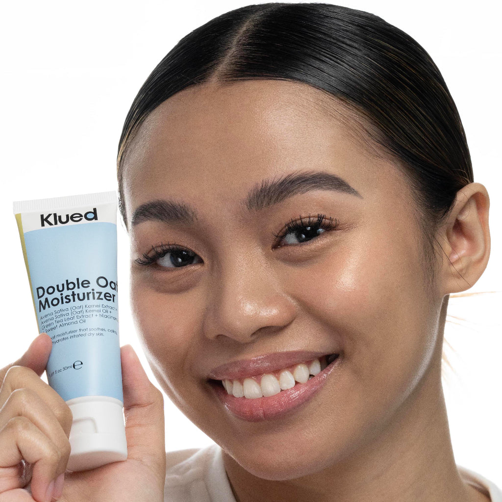 Woman holding a tube of Klued Double Oat Moisturizer against a white background