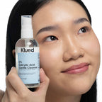 Person holding a bottle of Klued 2% Salicylic Acid Gentle Cleanser close to their face.