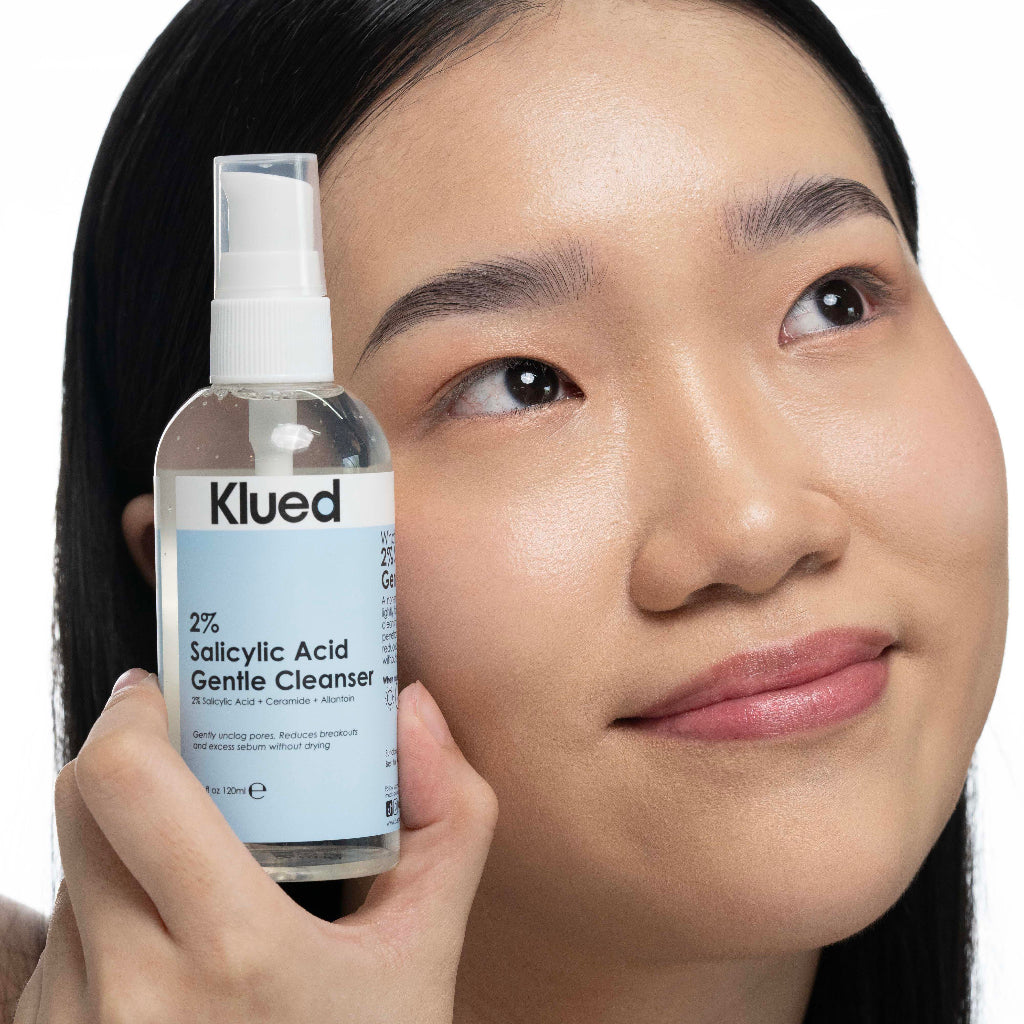 Person holding a bottle of Klued 2% Salicylic Acid Gentle Cleanser close to their face.