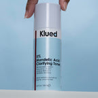 Klued 5% Mandelic Acid Clarifying Toner bottle held by a hand against a light blue background