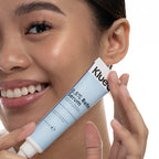 Woman holding a Klue serum tube close to her face on a white background