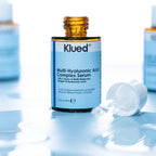 Klued Multi-Hyaluronic Acid Complex Serum bottle on a reflective surface with a blue gradient background